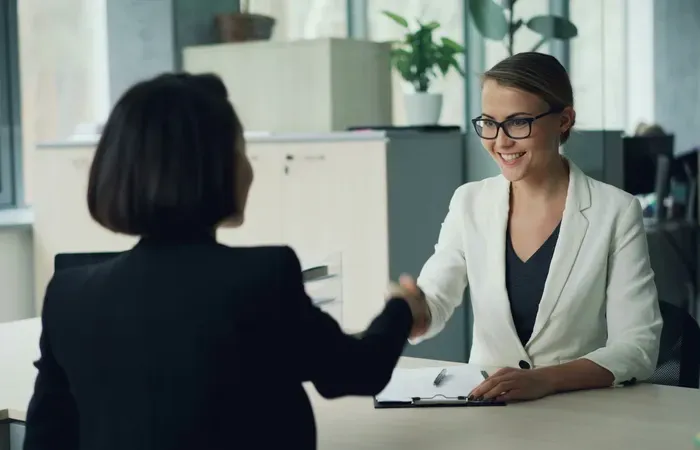 Two women smiling and shaking hands in an office meeting, reflecting trusted services on Local Biz Zone